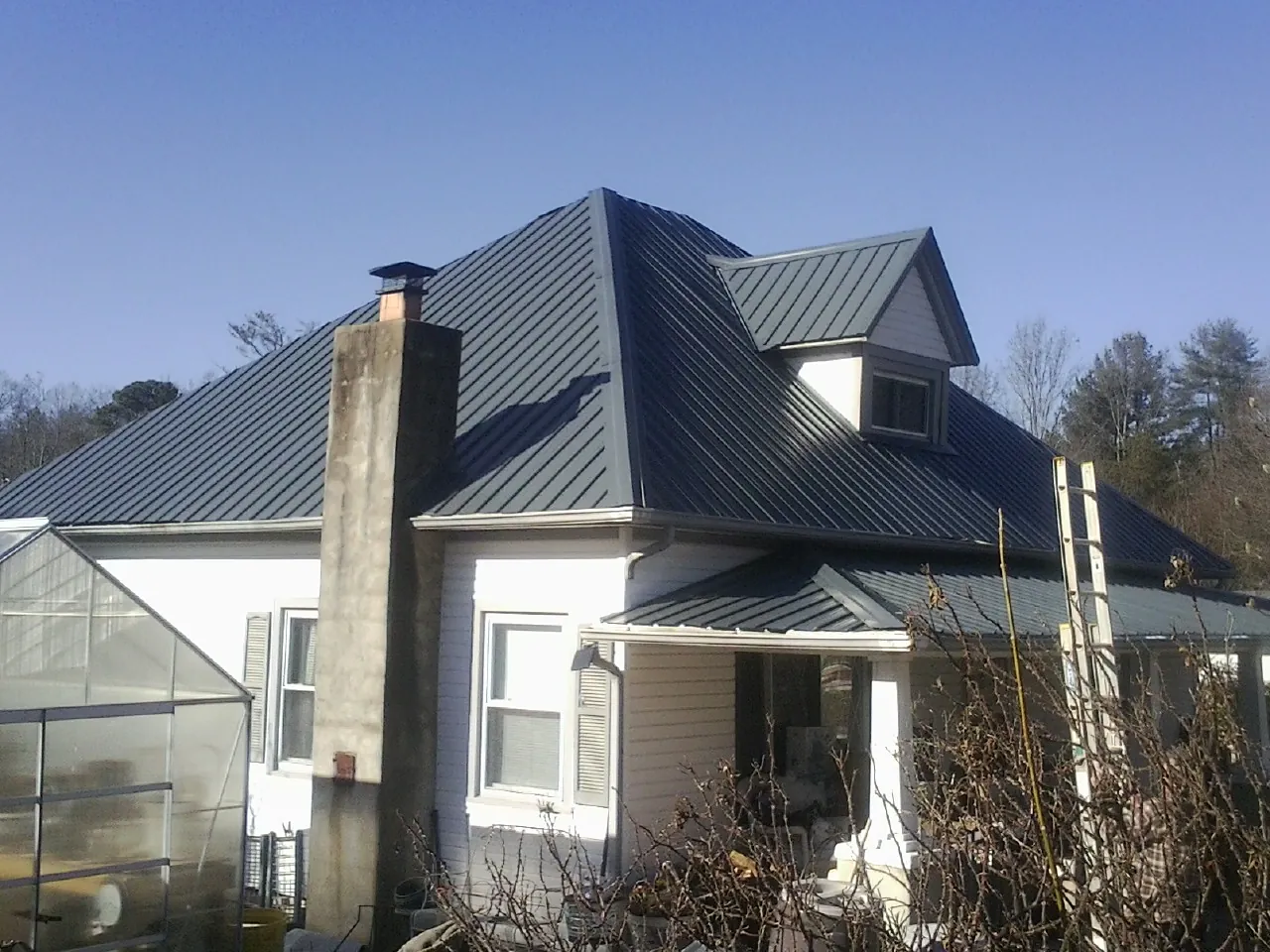 Dark blue standing seam metal roof on a white farmhouse with dormer — Slate & Tile Roof Repair by Roofing Brothers in Keller