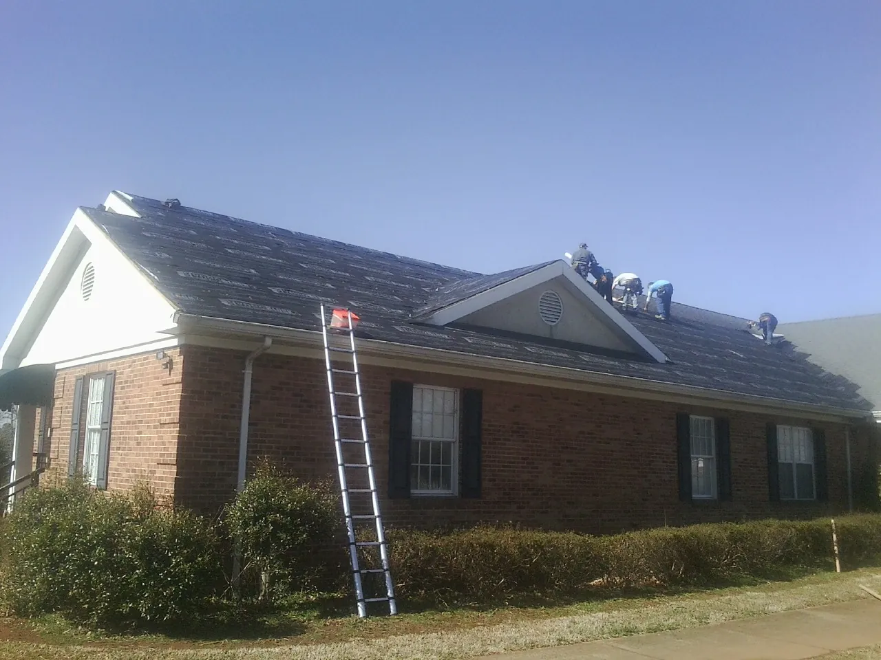 Crew tearing shingles off a brick ranch roof with a ladder set — Emergency Roof Repair work by our crew in Keller