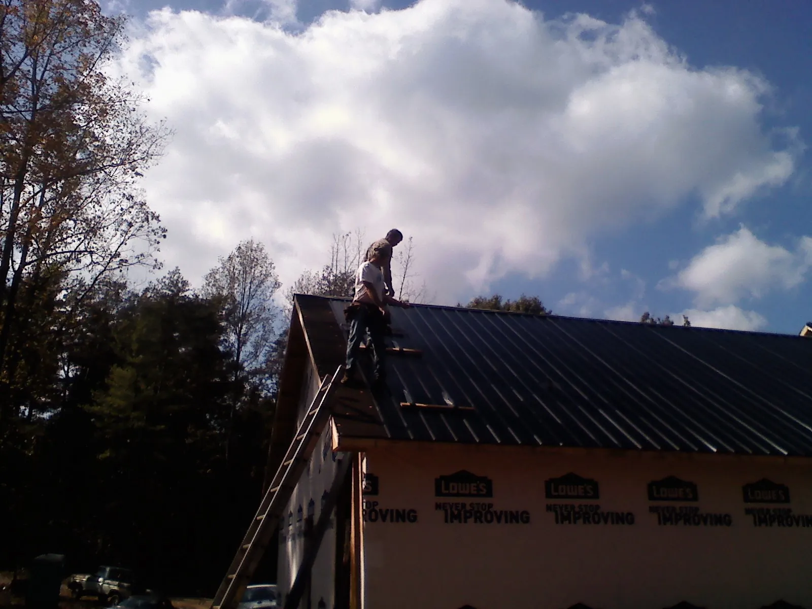 Roofer fastening dark metal panels high against a cloudy sky, from a Roof Inspection job in Keller